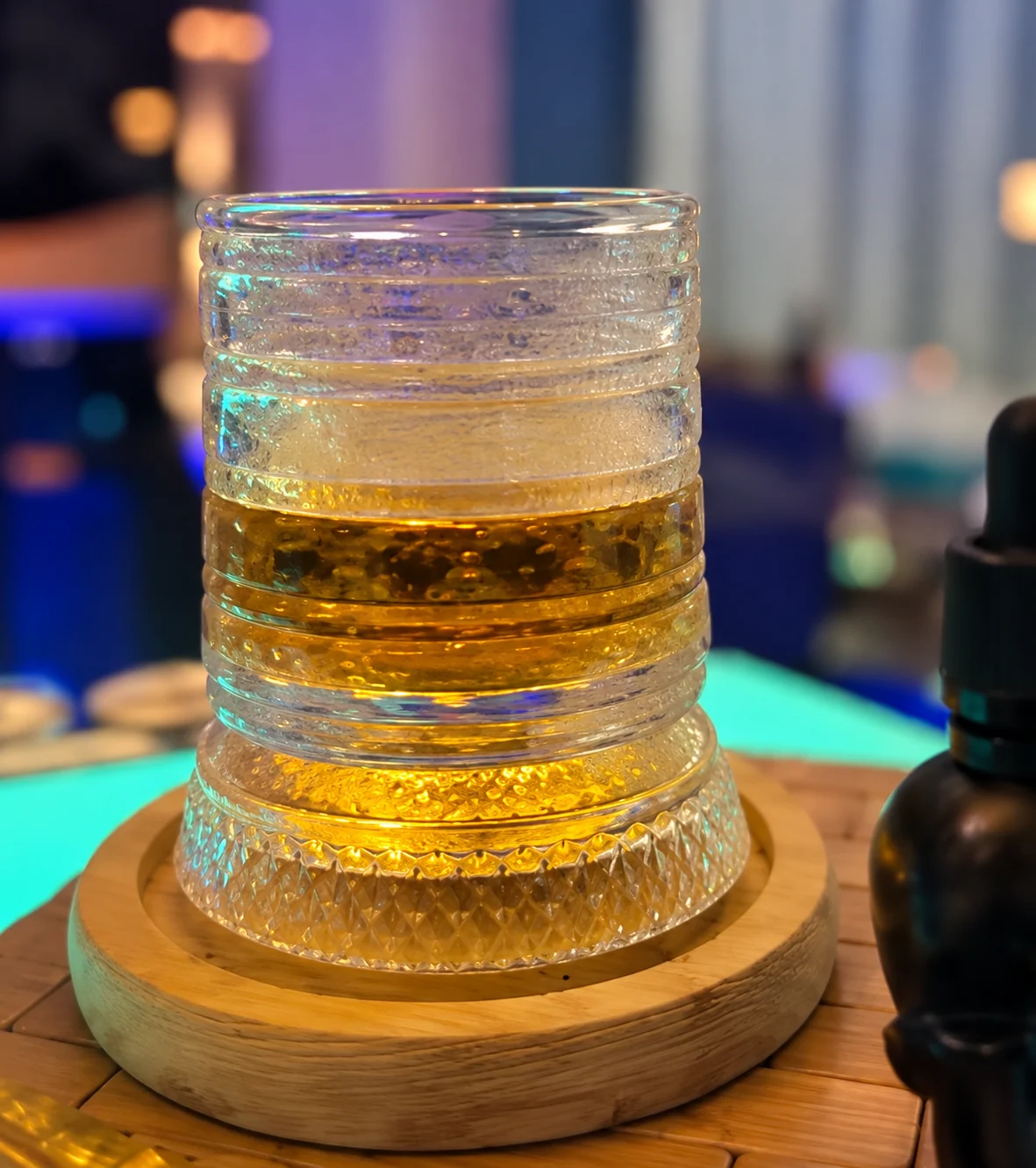 A layered drink displayed on a wooden stand at an evening event.