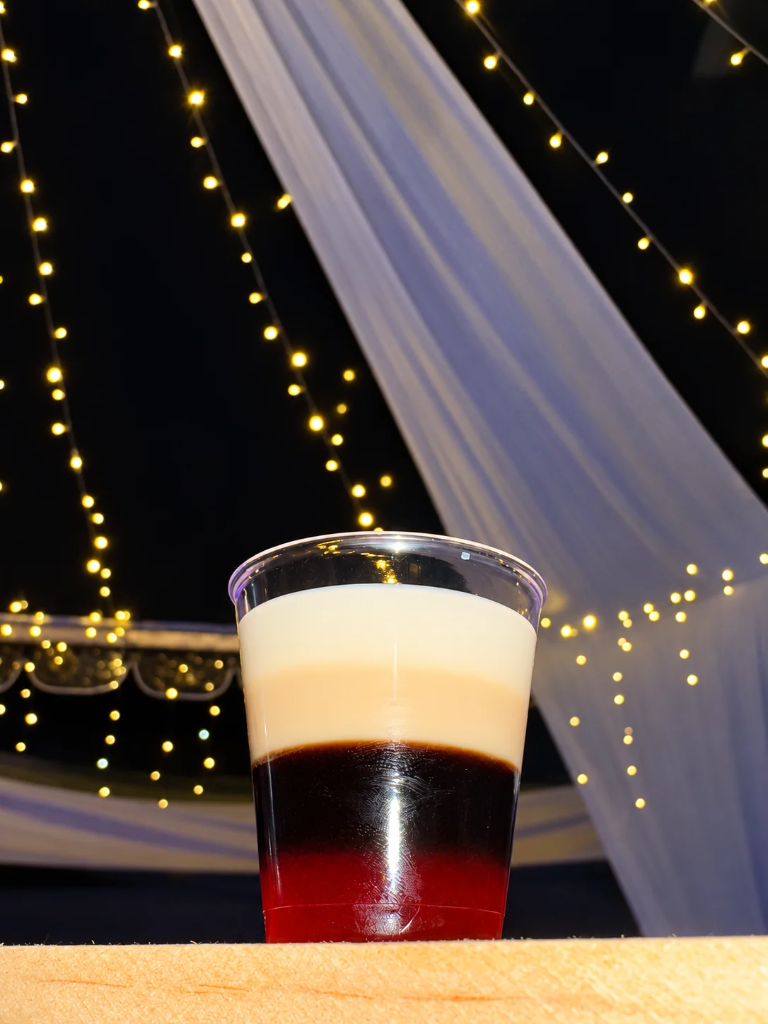 A red, dark and cream layered drink beneath warm event lights.