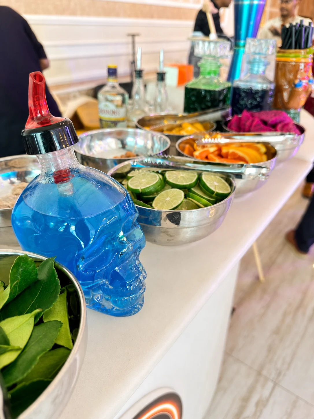 A blue skull-shaped bottle beside fresh citrus and garnish bowls on the bar.