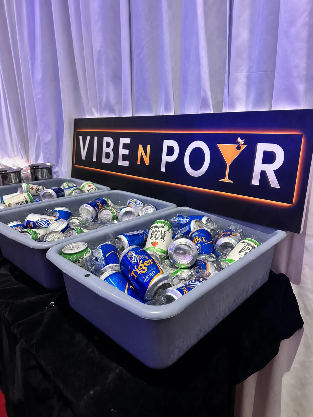 Beer and cider cans chilled on ice beneath a Vibe N Pour sign.