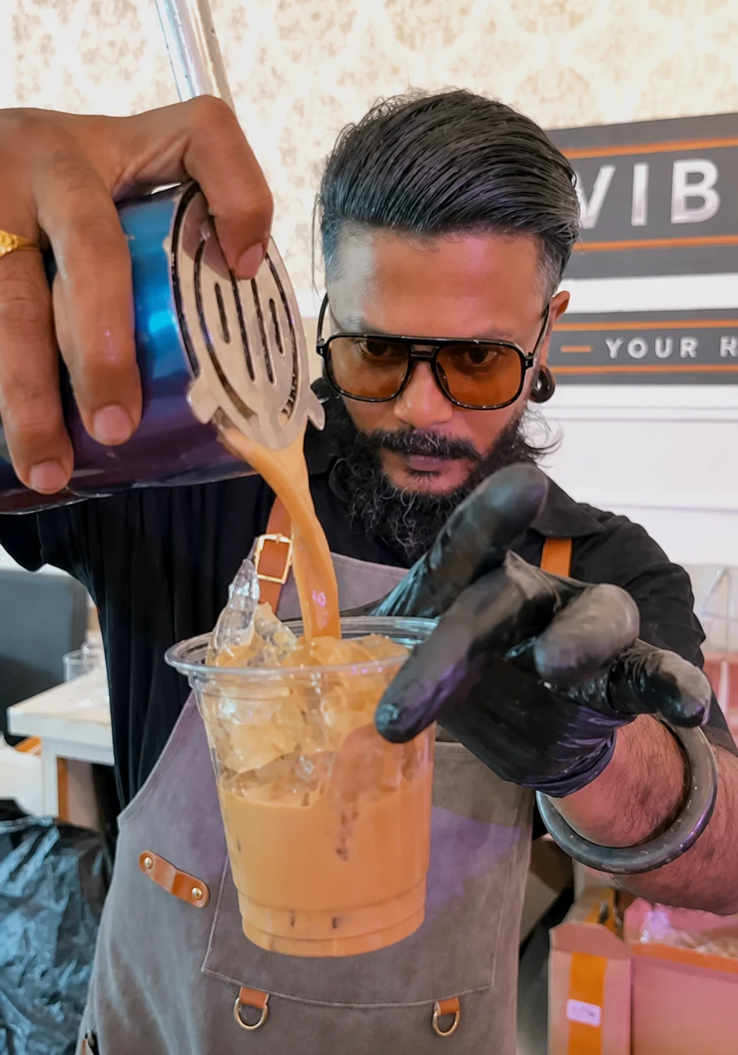 A bartender pouring an orange cocktail from a shaker into a cup of ice.